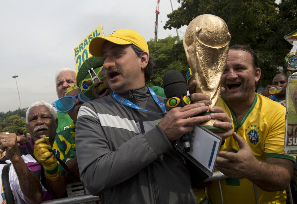 A Brazil soccer fan dressed in the likeness of coach Luiz Felipe Scolari, wearing a fake nose, holds a replica of the FIFA World Cup trophy as he poses for photos with fans outside the venue where Brazil's coach announced his squad for the upcoming international soccer tournament in Rio de Janeiro, Brazil, Wednesday, May 7, 2014. The team will mix talented young stars such as Neymar and Oscar with more experienced players such as Dani Alves, David Luiz, Thiago Silva and Hulk. Past stars such as Ronaldinho, Kaka and Robinho were left off the squad as expected. (AP Photo/Silvia Izquierdo)