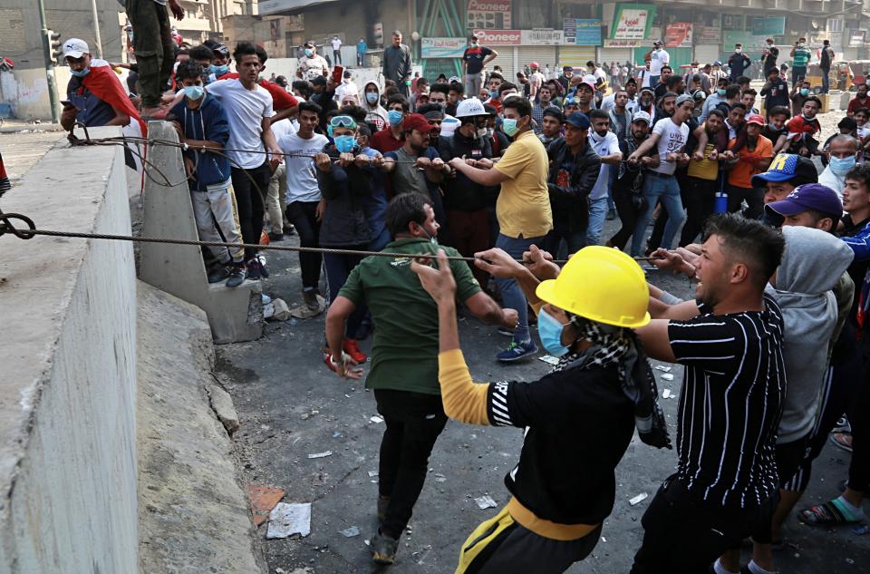 FILE - In this Sunday, Nov. 10, 2019 file photo, protesters try to pull down concrete barriers during clashes with Iraqi security forces in the Iraqi capital Baghdad. Iraq is rich in oil, but protesters say they don’t see the fruits of this wealth. Fueling the unrest, which began in October, is anger over an economy flush with oil money that has failed to bring jobs or improvements to the lives of young people, who are the majority of those taking to the streets. (AP Photo/Khalid Mohammed, File)