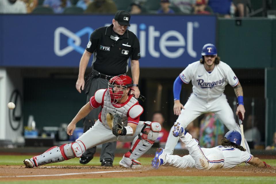 Philadelphia Phillies catcher J.T. Realmuto waits on the throw to the plate as Texas Rangers' Josh Smith scores on a single by Brad Miller in the second inning of a baseball game, Wednesday, June 22, 2022, in Arlington, Texas. Jonah Heim, right rear, who also scored on the single, and home plate umpire Chris Conroy, left rear, look on at the play,. (AP Photo/Tony Gutierrez)