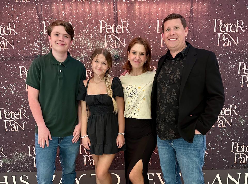 Terri Peters with her two kids and her husband standing in front of a step-and-repeat that says Peter Pan.