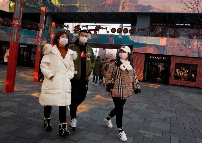 People wearing face masks walk past luxury boutiques in the Sanlitun shopping district in Beijing