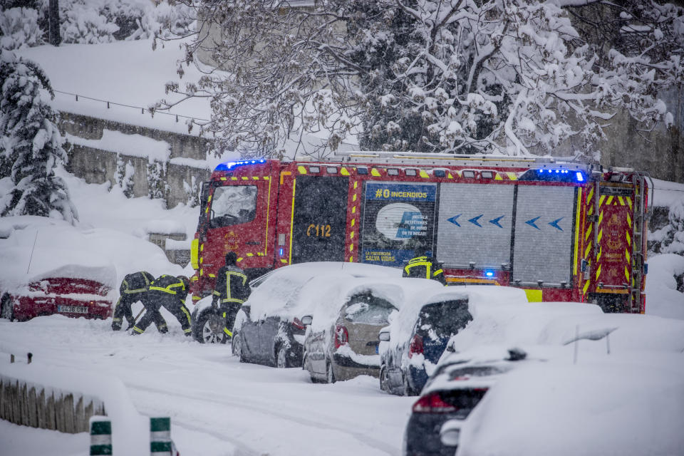 Firefighters work removing snow from a car during a heavy snowfall in Rivas Vaciamadrid, Spain, Saturday, Jan. 9, 2021. An unusual and persistent blizzard has blanketed large parts of Spain with snow, freezing traffic and leaving thousands trapped in cars or in train stations and airports that had suspended all services as the snow kept falling on Saturday. The capital, Madrid, and other parts of central Spain activated for the first time its red weather alert, its highest, and called in the military to rescue people from cars vehicles trapped in everything from small roads to the city's major thoroughfares. (AP Photo/Manu Fernandez)