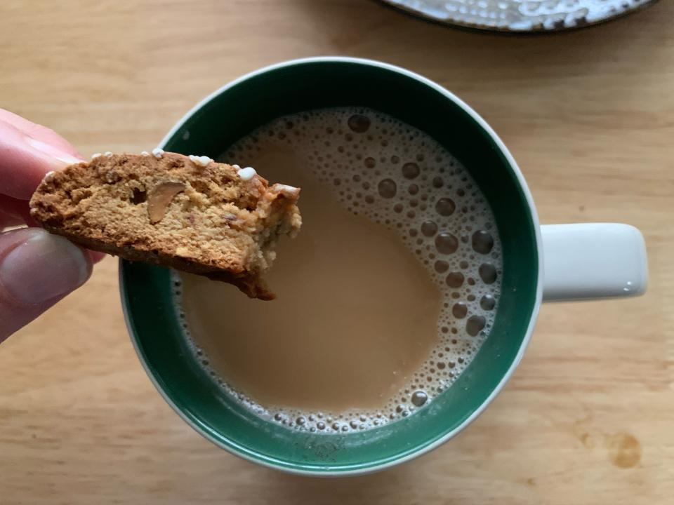 hand dipping mini trader joe's biscotti into white mug of coffee on wood table