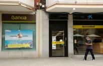 A man walks past branches of Bankia and Caixabank in Barcelona