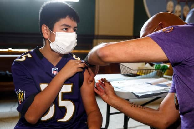 Dr. Barry Lavallee, CEO of Keewatinowi Inniniw Minoayawin, administers the Pfizer-BioNTech vaccine to Alexander Herrera, 14, at the Aboriginal Health and Wellness Centre in Winnipeg on Monday (Mike Deal/Winnipeg Free Press/The Canadian Press - image credit)