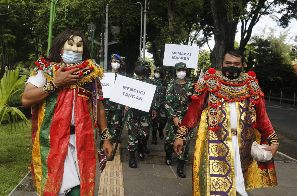 Indonesian military officers wear traditional Balinese costume calling for people to always have their mask and wash hands to prevent the spread of coronavirus outbreak on a street in Bali, Indonesia on Monday, Jan. 11, 2021. (AP Photo/Firdia Lisnawati)