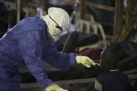 A health worker wearing protective equipment feeds a patient being treated for Ebola at the Island Clinic in Monrovia, September 30, 2014. REUTERS/Christopher Black/WHO/Handout via Reuters