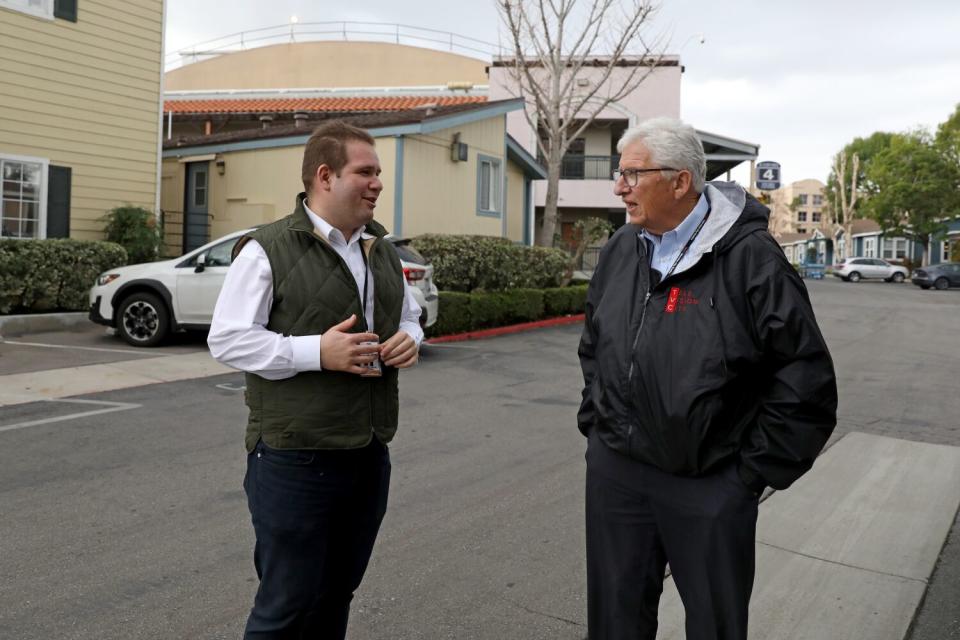 Two men stand talking outside on a residential-looking street