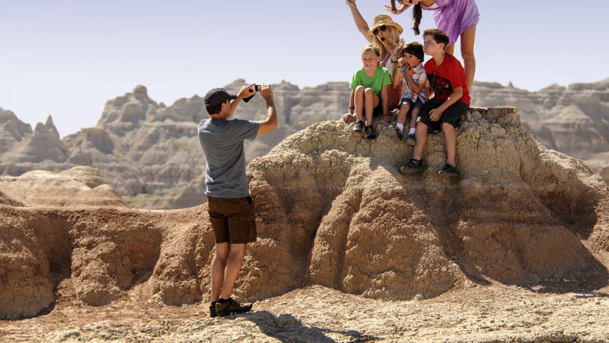 a family poses for a photo by a rock formation in badlands national park, a good housekeeping pick for best cheap places to travel