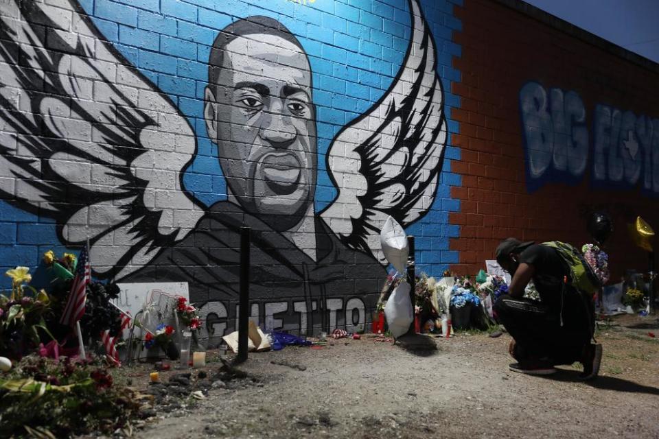 Joshua Broussard kneels in front of a memorial and mural that honors George Floyd in Houston, Texas.
