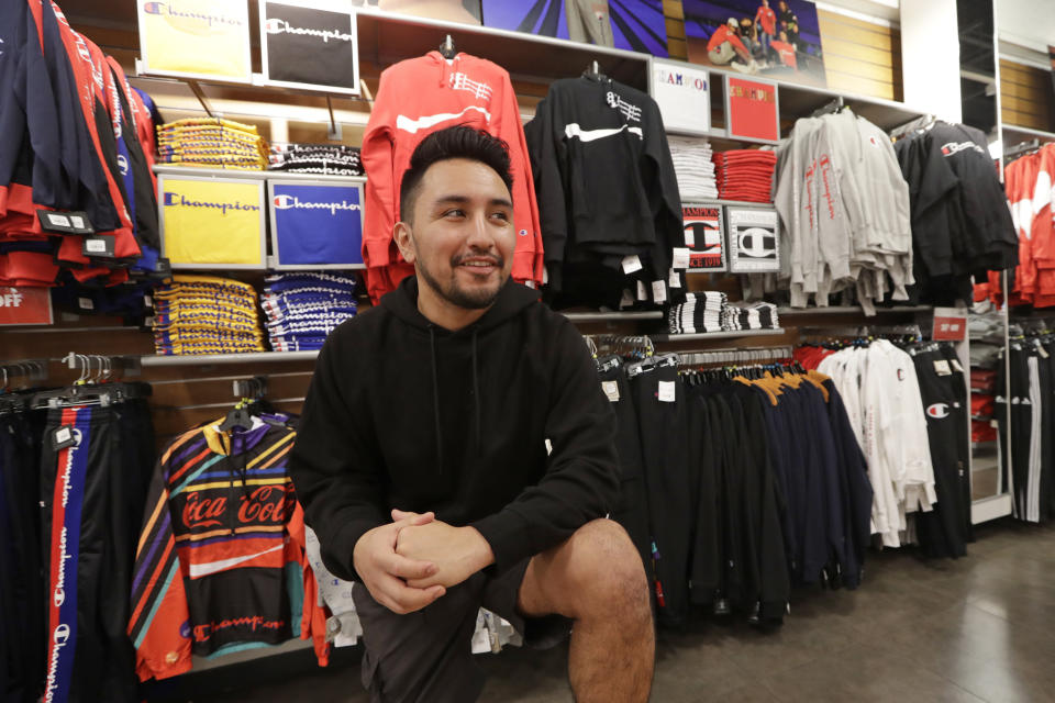 Victor Duran, a co-manager of a sports apparel store at the Southcenter mall, south of Seattle, poses for a photo at the store, Wednesday, Dec. 11, 2019, in Tukwila, Wash. Duran, 23, said he makes about $52,000 a year and doesn't get overtime, but is required to work at least 45 hours per week, and up to 60 during the holidays. Duran is one employee who could benefit from new overtime rules in Washington state, which will allow hundreds of thousands of workers who have been exempt to begin collecting when they work more than 40 hours per week. (AP Photo/Elaine Thompson)