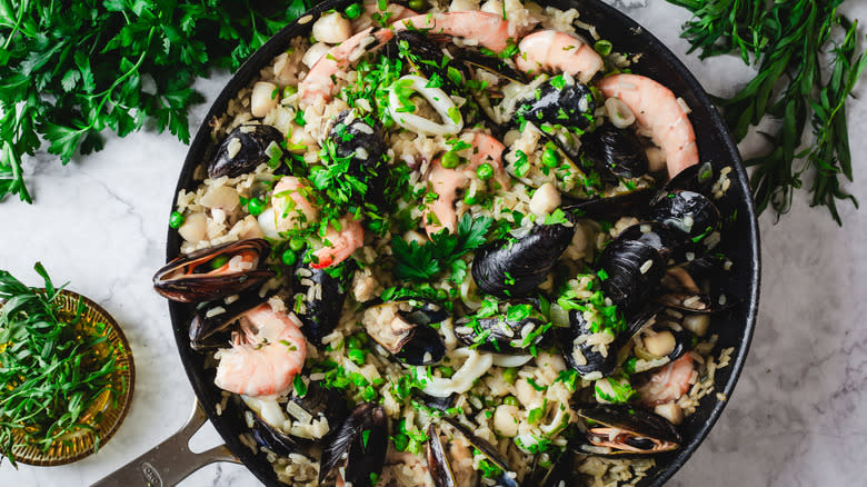 Pan of seafood risotto surrounded by herbs