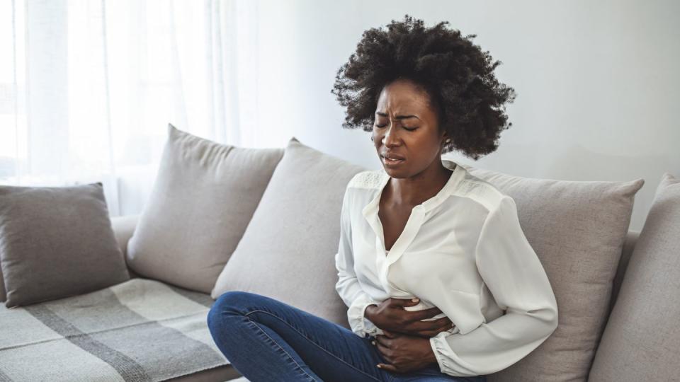 woman sitting on sofa suffering from stomach pain