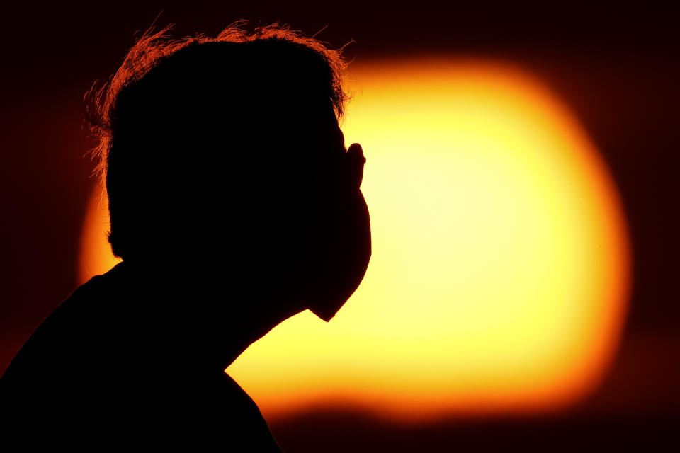 A man wearing a face mask to help prevent the spread of the coronavirus watches the sunset from a park in Kansas City, Mo., Friday, June 26, 2020. Sunsets and sunrises are more vibrant than usual lately due to dust in the atmosphere from a Saharan dust cloud. (AP Photo/Charlie Riedel)