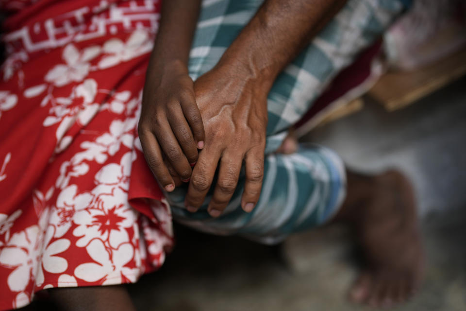 Jerifa Islam, left, holds the hand of her father Jaidul Islam as they spend time at a neighbor's home in a poor neighborhood in Bengaluru, India, Tuesday, July 19, 2022. In the suburban area where Jerifa and her family now live, most people are from Assam state, many forced to migrate because of climate change and dreaming of a better future. (AP Photo/Aijaz Rahi)