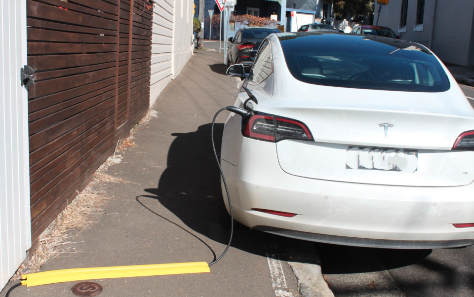 A white Tesla charges in a Balmain street with a cover over the wire on the footpath.