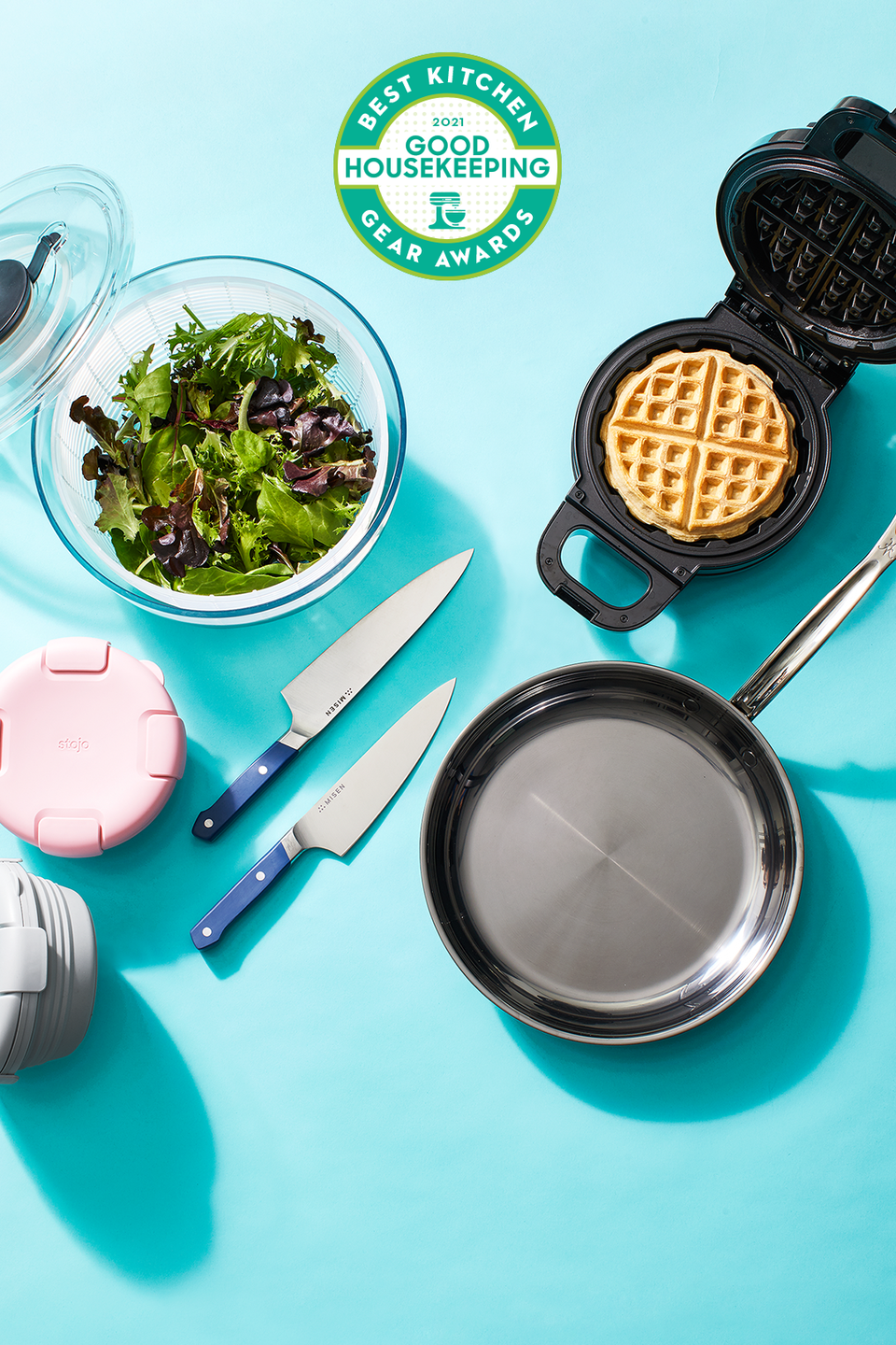 above view shot of kitchen appliances knives, frying pan, salad bowl and waffle maker with good housekeeping kitchen gear awards logo