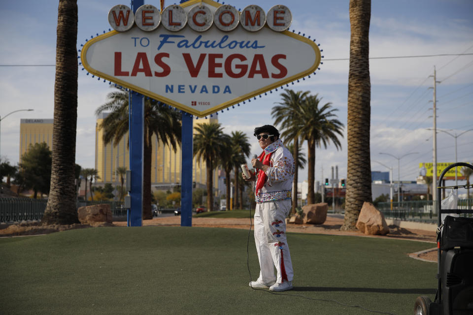 In this April 16, 2020, photo, Chris Morehouse drinks a beer while performing as Elvis at the "Welcome to Fabulous Las Vegas Nevada" sign along the Strip in Las Vegas. "I'm just singing for the sign," said Morehouse who was at times performing save the few locals who occasionally took advantage of the eerie silence to take photos at the sign. (AP Photo/John Locher)