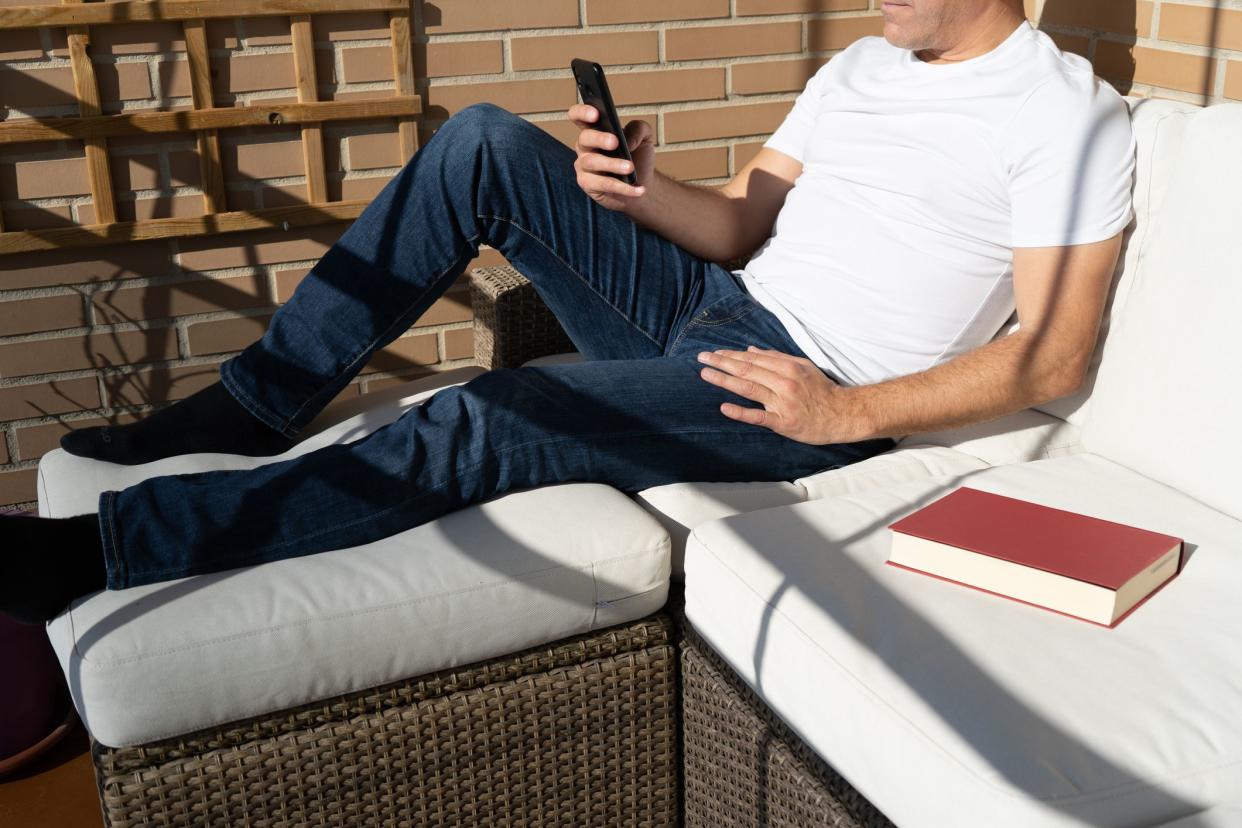 Man lying on a terrace using a smartphone with a book next to him. Relax at home