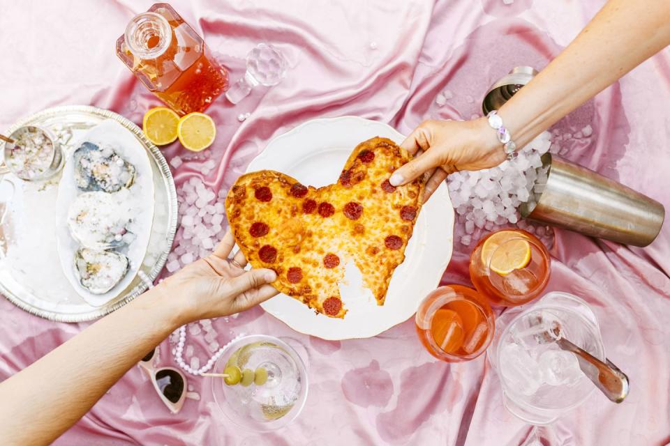 friends pulling heart shaped pepperoni pizza at table