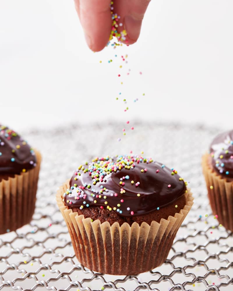 someone is dropping sprinkles on to the chocolate cupcakes