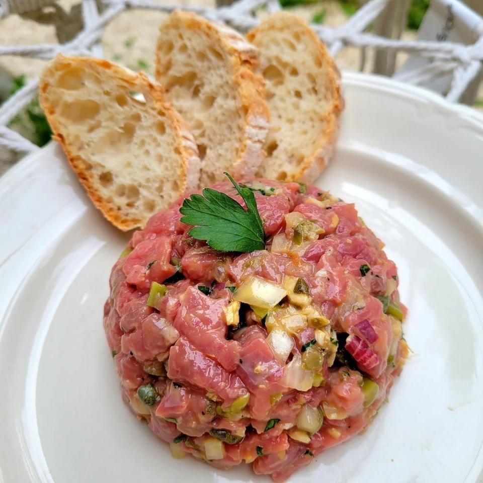 Tuna tartare topped with parsley, served on a white plate with three slices of baguette