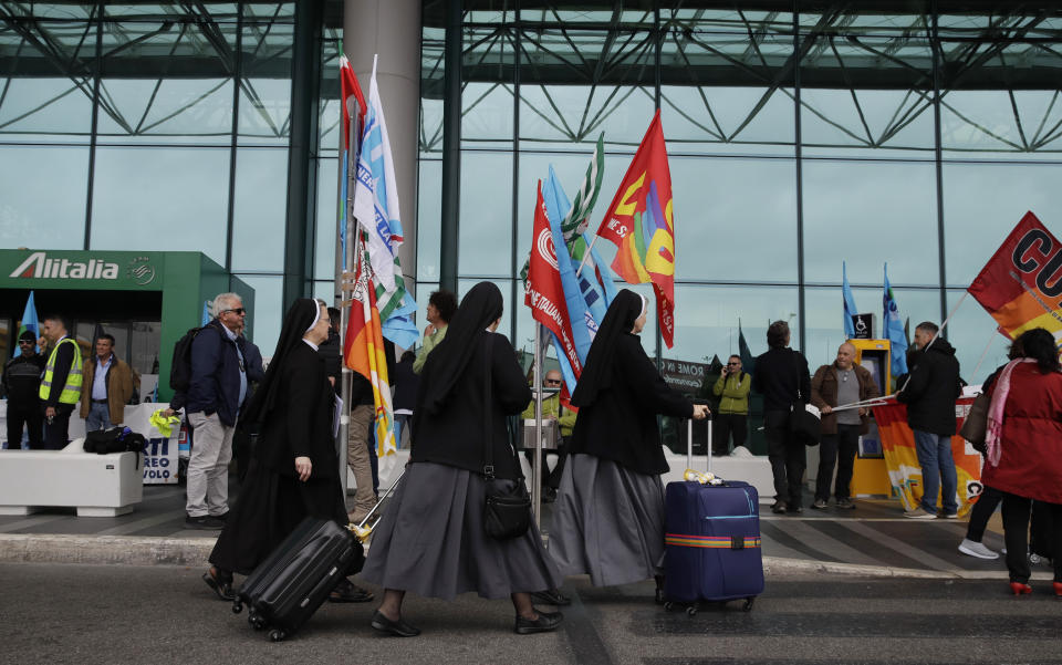 Nuns and other passengers pass in front of striking Alitalia workers with unions flags and banners, at the Fiumicino airport in Rome Tuesday, May 21, 2019. Alitalia workers are on a 24 hours strike since Monday night. (AP Photo/Alessandra Tarantino)