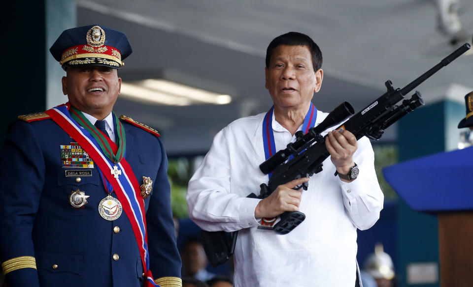 FILE - In this April 19, 2018 file photo, Philippine President Rodrigo Duterte, right, jokes to photographers as he holds an Israeli-made Galil rifle which was presented to him by former Philippine National Police Chief Director General Ronald Dela Rosa at the turnover-of-command ceremony at the Camp Crame in Quezon city northeast of Manila. Elections officials were to proclaim the winners Wednesday, May 22, 2019, after finishing the official count of the May 13 elections overnight. President Duterte backed eight winning aspirants to half of the seats in the 24-member Senate, including his former national police chief, Dela Rosa, who enforced the president's crackdown on illegal drugs in a campaign that left thousands of suspects dead and drew international condemnation. (AP Photo/Bullit Marquez, File)