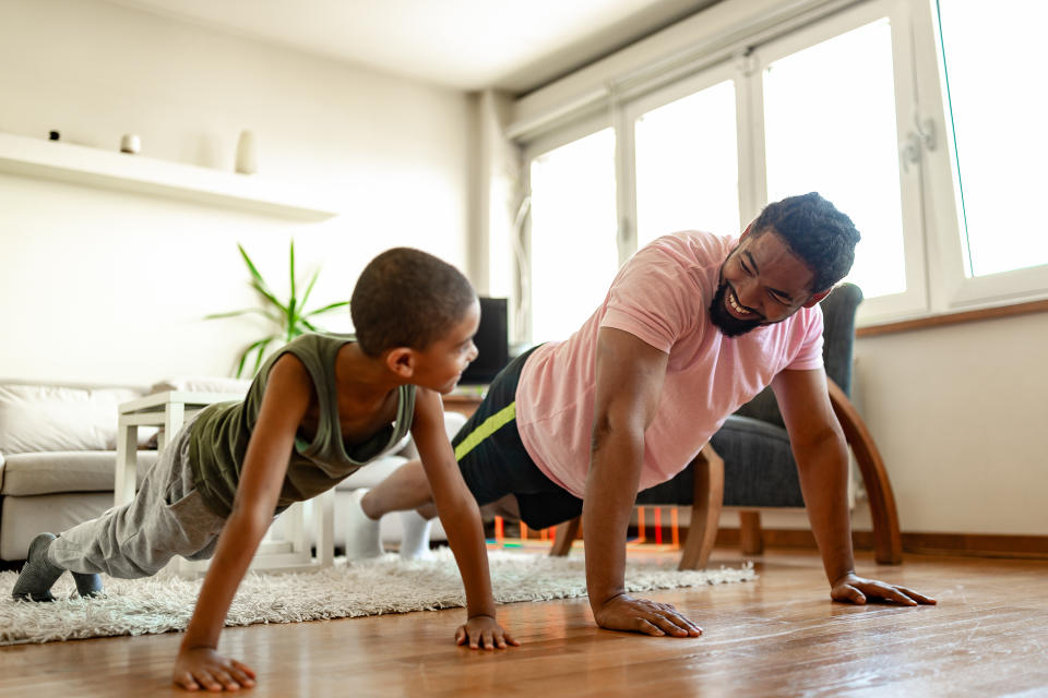A father and son are exercising at home, doing a plank while smiling at each other