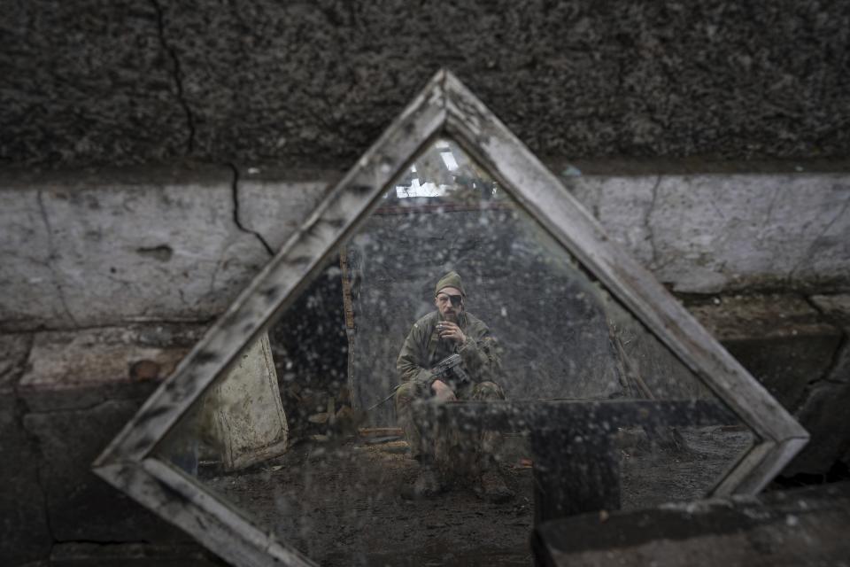 A Ukrainian serviceman is reflected in a mirror as he smokes a cigarette on a position at the line of separation between Ukraine-held territory and rebel-held territory near Zolote, Ukraine, Saturday, Feb. 19, 2022. Ukrainian President Volodymyr Zelenskyy, facing a sharp spike in violence in and around territory held by Russia-backed rebels and increasingly dire warnings that Russia plans to invade, has called for Russian President Vladimir Putin to meet him and seek a resolution to the crisis. (AP Photo/Evgeniy Maloletka)