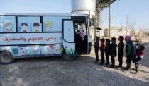 Sudents wait in line to attend a class inside a bus in the city of al-Bab