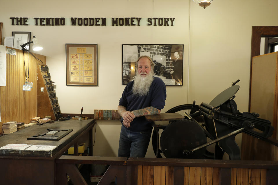 In this May 21, 2020 photo, Loren Ackerman leans on an 1890s-era press he uses to print wooden money in Tenino, Wash. In an effort to help residents and local merchants alike get through the economic fallout of the coronavirus pandemic, the small town has issued wooden currency for residents to spend at local businesses, decades after it created a similar program during the Great Depression. (AP Photo/Ted S. Warren)
