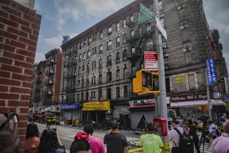 Onlookers view the aftermath of a fire which authorities say started at an e-bike shop and spread to upper-floor apartments, Tuesday June 20, 2023, in New York. (AP Photo/Bebeto Matthews)