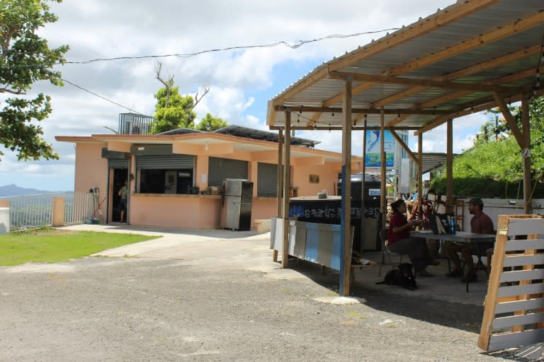 Two people are seen seated in a community kitchen that served up to 400 meals a day after Hurricane Maria hit Puerto Rico; a year later the numbers have dwindled to 20 a day but volunteers are keeping it going