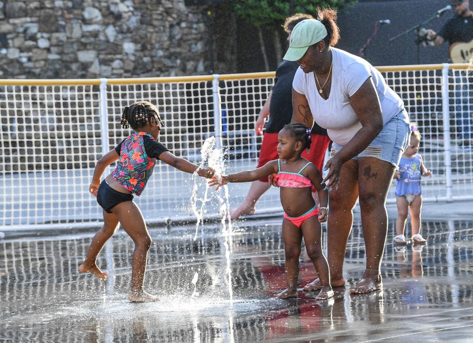 Kia Bell, right, of Anderson lets daughters London Smith, middle, and Skylar Simmons, left, play in the water of a splash pad at Carolina Wren Park during the Piedmont Natural Gas Main Street Program Block Party in Anderson, S.C. Thursday, July 8, 2021. Rain from Hurricane Elsa passed through in the morning and cleared the way for the weekly downtown Block Party. 