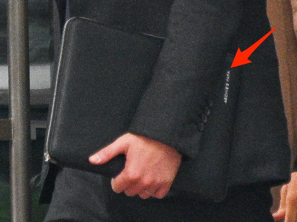 A photo of Prince Harry carrying a folio that says "Archie's Papa" on it with an arrow pointing to the engraving.