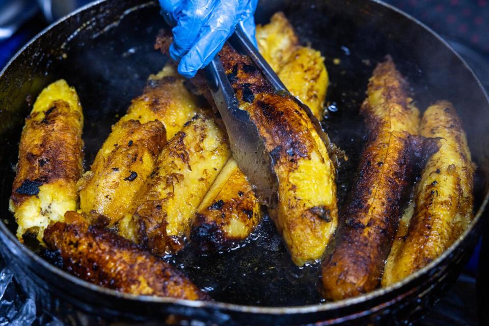 Tina Tunay cooks "platanos fritos" on a makeshift grill set up on the sidewalk