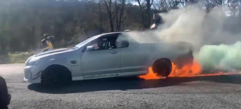 A white Holden ute does a burnout in Canberra with the back of the car lighting on fire.