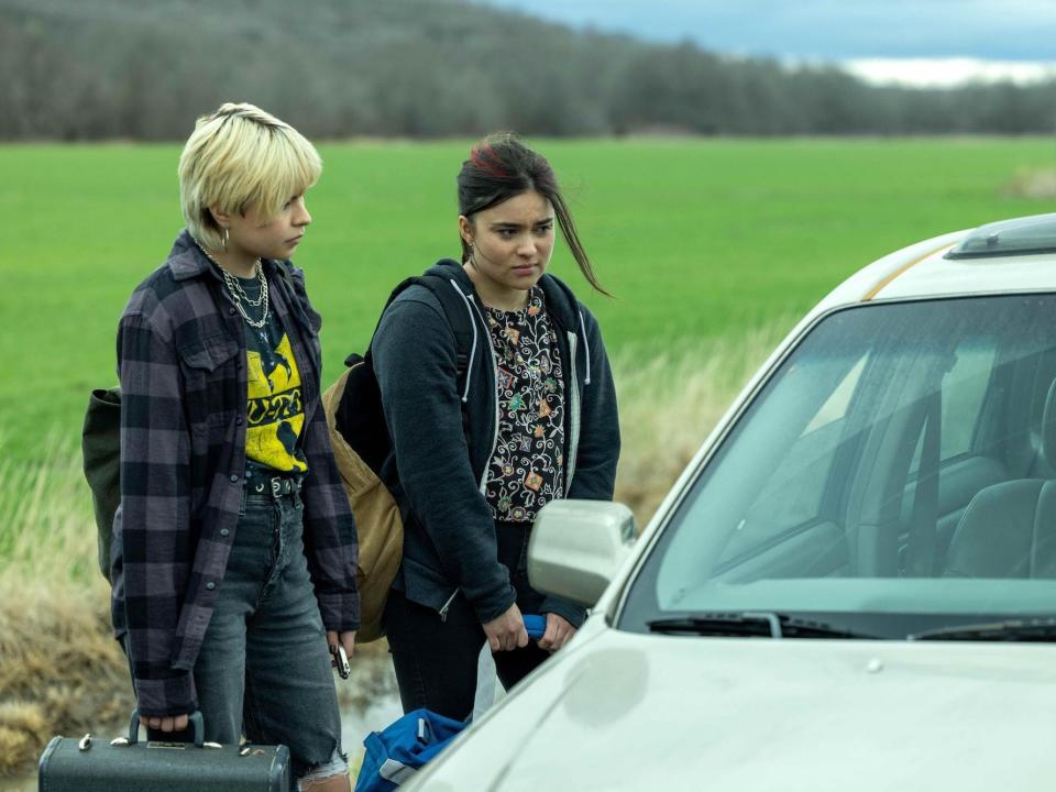 Two young teens standing outside a car by a field.