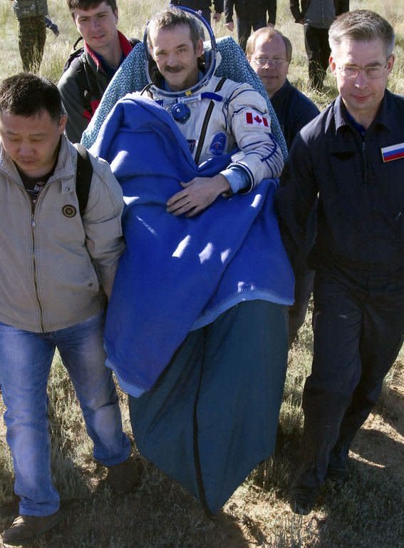 Russian space agency personnel carry Canadian astronaut Chris Hadfield (C) after his landing aboard the Russian Soyuz space capsule in Kazakhstan on May 14, 2013 .Hadfield returned to Earth along with two other astronauts after a half-year mission to the International Space Station that saw him shoot to global stardom through his Twitter microblog