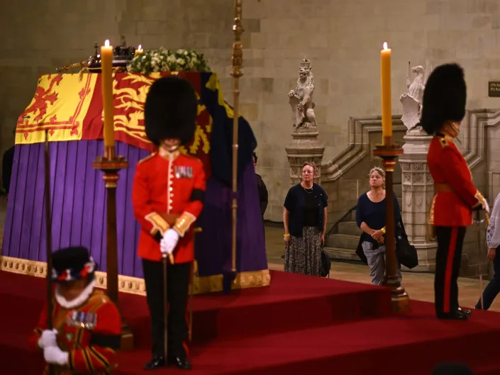 Royal guards wearing bearskin hats stand in front of the Queen's coffin.