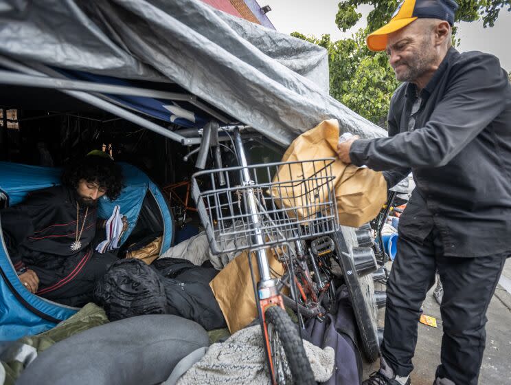 Los Angeles, CA - May 19: Oscar Magana, 22, left, who struggles with mental problems but does not use drugs, sits in his tent as his step father, Johnny Roman, right, 58, who is addicted to meth, bipolar, manic depressive, and ADHD, puts bags of supplies for drug use in their tent encampment near Avalon Boulevard and East Florence Avenue in South Los Angeles Friday, May 19, 2023. The bags of supplies were distributed by a team from Homeless Outreach Program Integrated Care Systems [HOPICS] and includes drug pipes, overdose reversal nasal spray, fentanyl test strips, wipes and educational materials are aimed at preventing infection and disease, and saving them from the fentanyl death crisis. (Allen J. Schaben / Los Angeles Times)