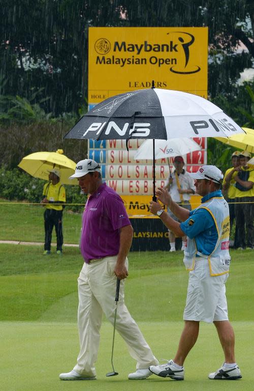 Lee Westwood takes cover under an umbrella as it rains during the final round of the Malaysian Open golf tournament in Kuala Lumpur on April 20, 2014