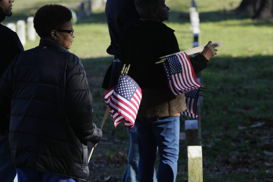 Thelma Sims Dukes, right, and her niece Sara Sims, left, are escorted by reenactors as they carry American flags to be placed by the graves of Civil War soldiers of the United States 1st Mississippi Infantry (African Descent) in Vicksburg National Cemetery, Feb. 14, 2024, in Vicksburg, Miss. Thirteen flags were placed at the graves of Black soldiers killed in an 1864 massacre at Ross Landing, Arkansas, who were buried as unknowns but have recently been identified. (AP Photo/Rogelio V. Solis)