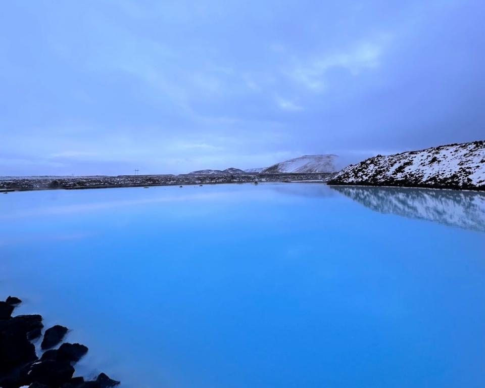 A large body of water surrounded by snow mountains and a dark-blue sky with clouds overhead