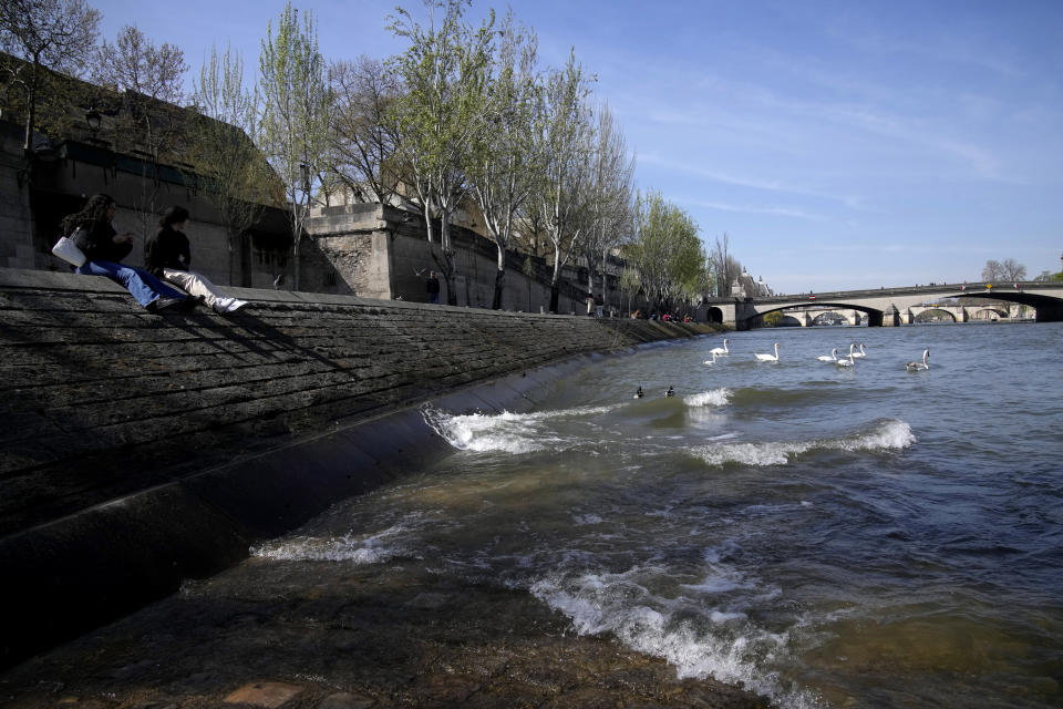 People relax along the River Seine waterbanks in Paris, Wednesday, April 5, 2023. A costly and complex clean-up is resuscitating the River Seine just in time for it to play a starring role in the 2024 Paris Olympics. The city and its region are rushing to make the Seine's murky waters swimmable, so it can genuinely live up to its billing as the world’s most romantic river. (AP Photo/Christophe Ena)