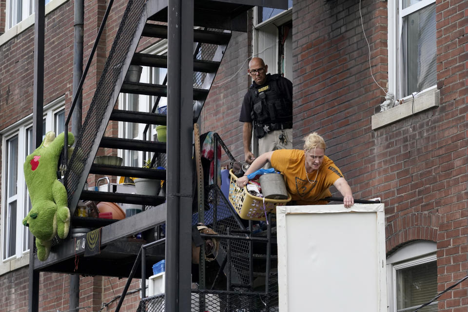 Kristen Bigogno tosses some of her belongings off a balcony as a member of the St. Louis Sheriff's Department watches as Bigogno is evicted from her home Friday, Sept. 17, 2021, in St. Louis. Bigogno is among thousands of Americans facing eviction now that the national moratorium has ended. (AP Photo/Jeff Roberson)