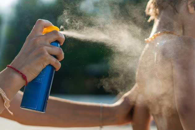 A mother sprays sunscreen on her son's body at the beach.