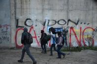 Migrants with luggage walk past a graffiti on a wall reading "London calling", as they leave the "Jungle" migrant camp in Calais, northern France, on October 24, 2016