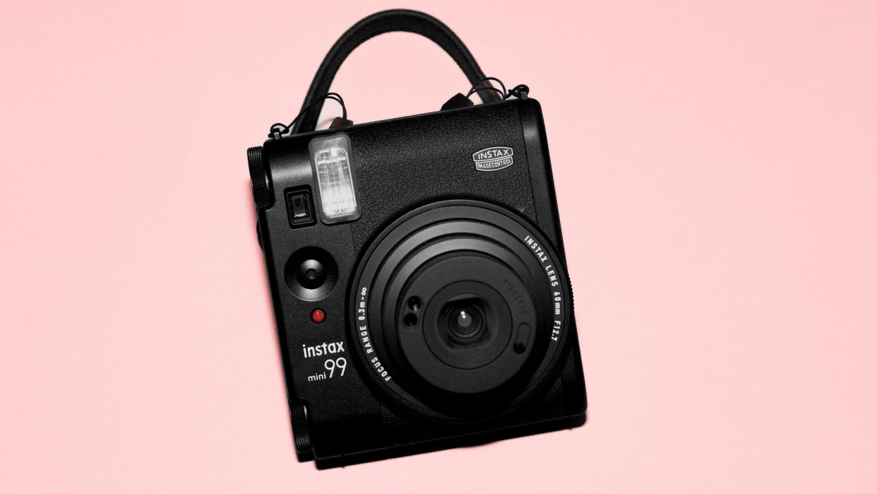  A photograph of the Fujifilm Instax mini 99 in black, set against a pink background. 